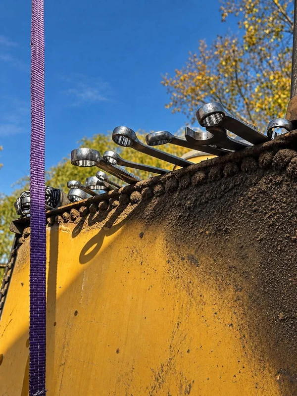 Row of hydraulic hose fittings across the top of a yellow machine, held up by a purple lifting strap